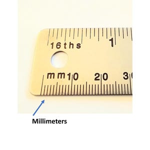 May include: A silver-toned metal ruler featuring black markings for both inches and millimeters. The top edge displays 16ths of an inch, while the bottom edge shows millimeter increments labeled with the text mm, 10, 20, and 30.
