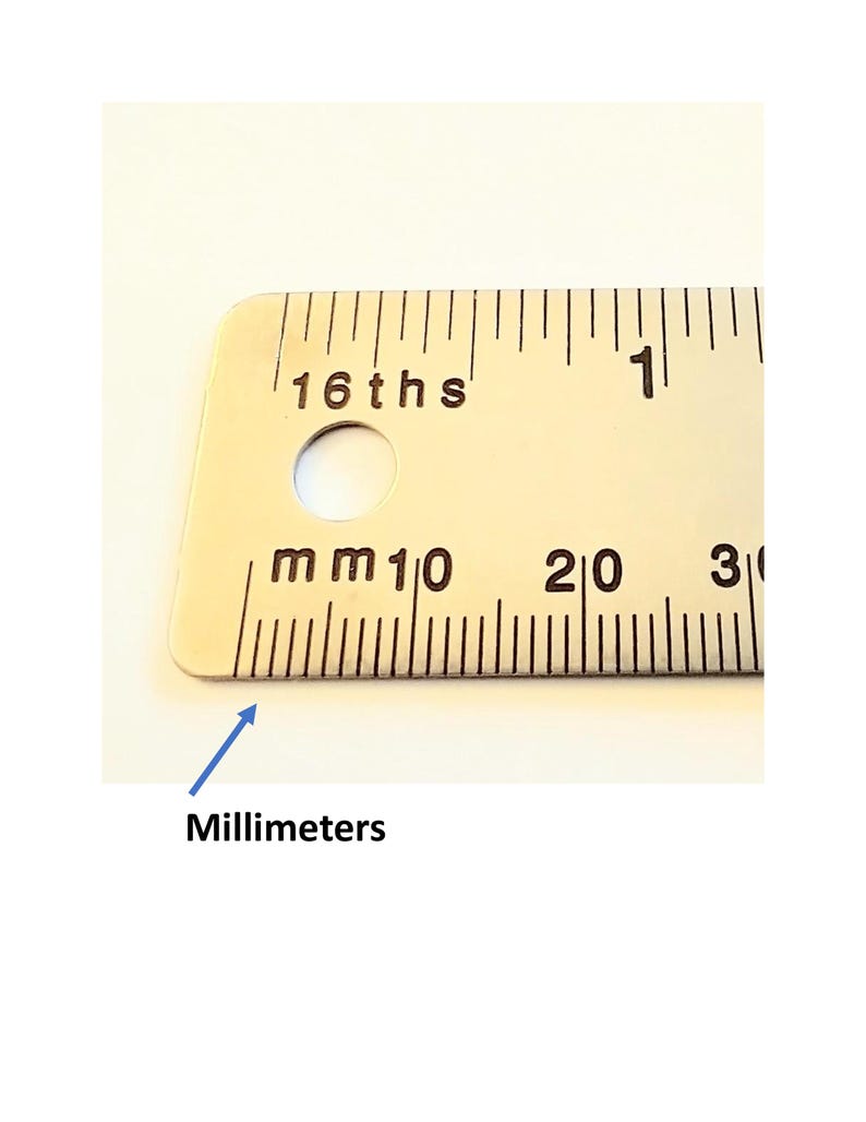 May include: A silver-toned metal ruler featuring black markings for both inches and millimeters. The top edge displays 16ths of an inch, while the bottom edge shows millimeter increments labeled with the text mm, 10, 20, and 30.