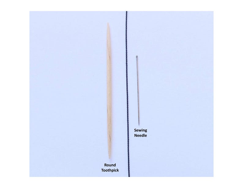 May include: A light-colored wooden round toothpick positioned vertically next to a thin silver-colored metal sewing needle. A thin black vertical line separates the two items. The text Round Toothpick and Sewing Needle is printed below them.
