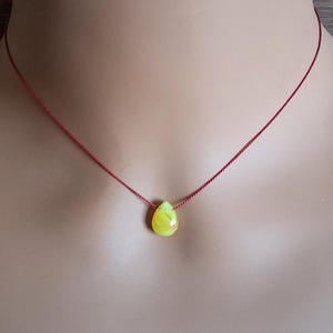 May include: A necklace featuring a single, small, teardrop-shaped pendant in a vibrant yellow and lime green marbled pattern, suspended on a thin, simple red cord that rests against the neck, creating a minimalist and colorful jewelry piece.