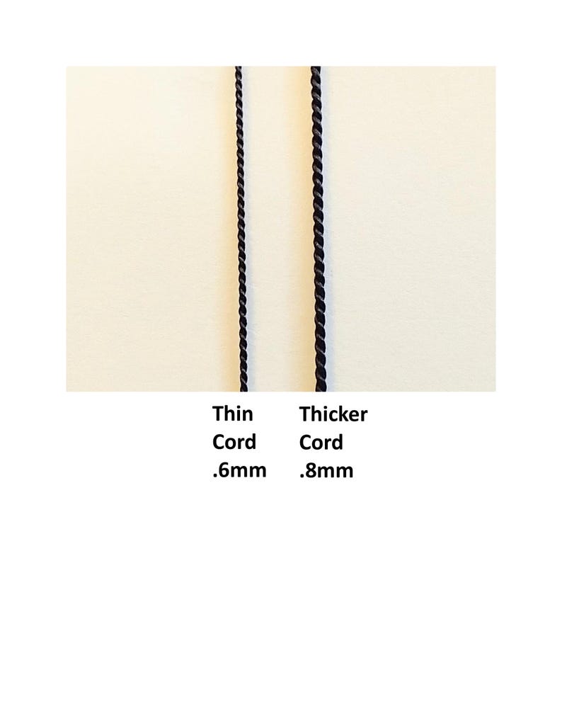 May include: Two black twisted cords displayed vertically. The left cord is labeled Thin Cord .6mm and the right cord is labeled Thicker Cord .8mm. The cords have a uniform, spiraled texture and are positioned side by side against a plain background.