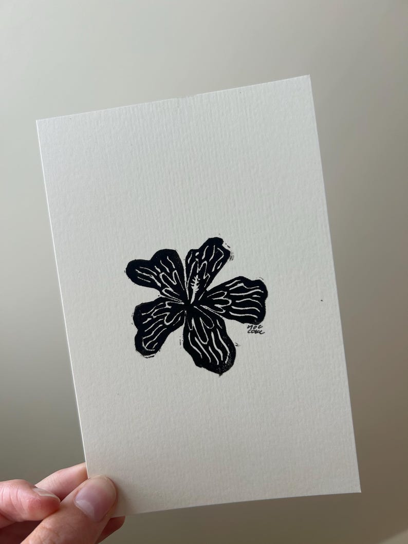 Puede incluir: Un grabado en lin&oacute;leo en blanco y negro de una flor de cinco p&eacute;talos sobre papel crema. La flor es el punto focal, con una apariencia texturizada. La firma del artista est&aacute; en la esquina inferior derecha. La impresi&oacute;n es sobre papel crema.