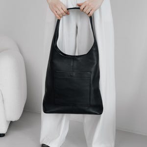 Könnte beinhalten: Eine schwarze Ledertasche mit einer einzigen Tasche auf der Vorderseite. Die Tasche hat einen langen Riemen und wird über der Schulter getragen.