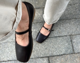 May include: A pair of black leather mary jane shoes with a buckle strap. The shoes have a square toe and a low heel.