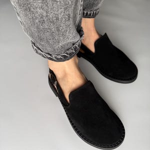 Peut inclure: Une paire de chaussures à enfiler en daim noir avec une bride à l'arrière. Les chaussures ont une pointe arrondie et une semelle plate.