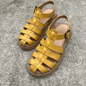 May include: A pair of yellow leather sandals with a caged design and a buckle closure. The sandals have a thick, flat sole.