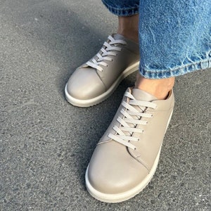 May include: A pair of light beige leather low-top sneakers with white laces and a white rubber sole.