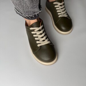 May include: A pair of olive green leather low-top sneakers with white laces. The sneakers have a white rubber sole.