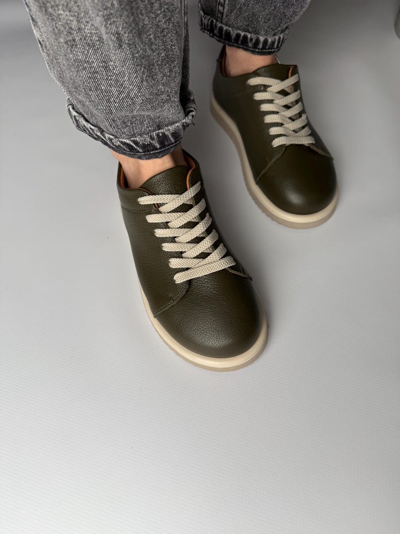 May include: A pair of olive green leather low-top sneakers with white laces. The sneakers have a white rubber sole.