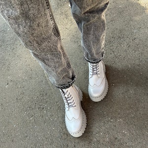 May include: White leather lace-up boots with a chunky platform sole and brogue detailing. The boots are worn with distressed denim jeans.