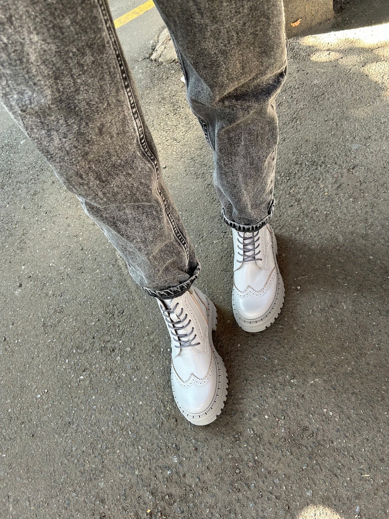 May include: White leather lace-up boots with a chunky platform sole and brogue detailing. The boots are worn with distressed denim jeans.