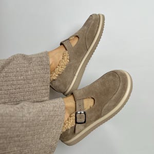 Puede incluir: Un par de zapatos de ante marr&oacute;n claro con cierre de hebilla y forro de piel sint&eacute;tica. Los zapatos tienen una suela de goma blanca.