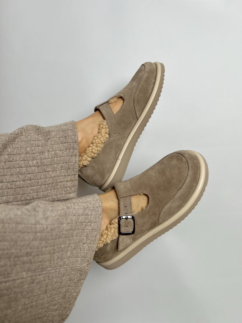 Puede incluir: Un par de zapatos de ante marr&oacute;n claro con cierre de hebilla y forro de piel sint&eacute;tica. Los zapatos tienen una suela de goma blanca.
