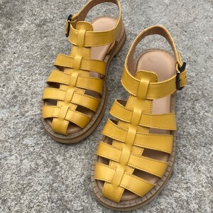 May include: A pair of yellow leather sandals with a caged design and buckle closures. The sandals have a thick, flat sole.