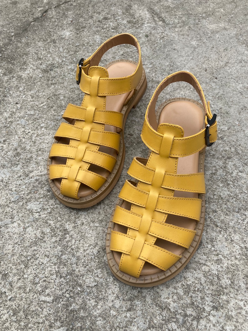 May include: A pair of yellow leather sandals with a caged design and buckle closures. The sandals have a thick, flat sole.