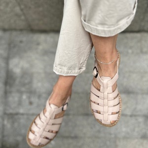 May include: A pair of light pink leather sandals with a caged design. The sandals have a buckle closure and a flat sole.