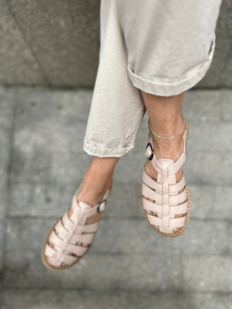 May include: A pair of light pink leather sandals with a caged design. The sandals have a buckle closure and a flat sole.