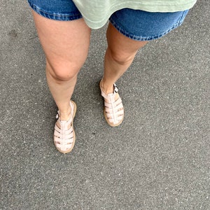 May include: A pair of pink gladiator sandals with a buckle closure. The sandals are made of a woven material and have a flat sole.