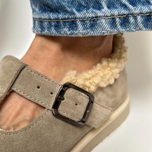 Puede incluir: Un par de zapatos de ante marr&oacute;n claro con cierre de hebilla y forro de piel sint&eacute;tica. Los zapatos tienen una suela de goma blanca.