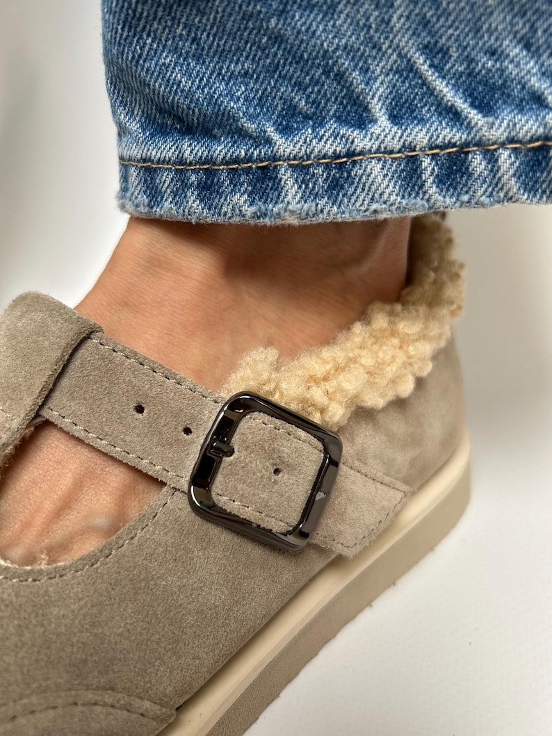 Puede incluir: Un par de zapatos de ante marr&oacute;n claro con cierre de hebilla y forro de piel sint&eacute;tica. Los zapatos tienen una suela de goma blanca.