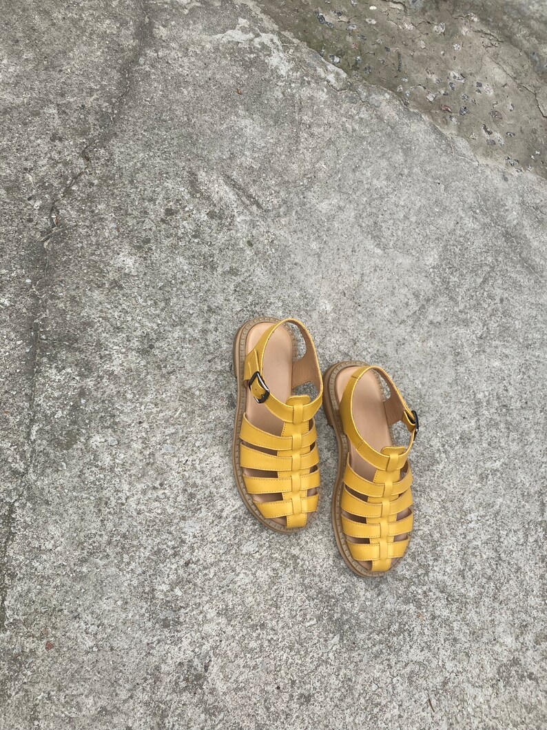May include: A pair of yellow leather sandals with a woven design. The sandals have a buckle closure and a flat sole.