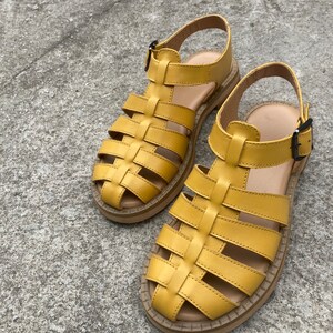 May include: A pair of yellow leather sandals with a caged design. The sandals have a thick sole and a buckle closure.