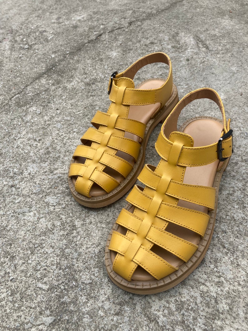May include: A pair of yellow leather sandals with a caged design. The sandals have a thick sole and a buckle closure.