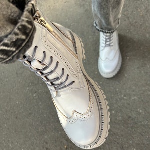 May include: White leather boots with a zipper and laces. The boots have a brogue design and a chunky sole.