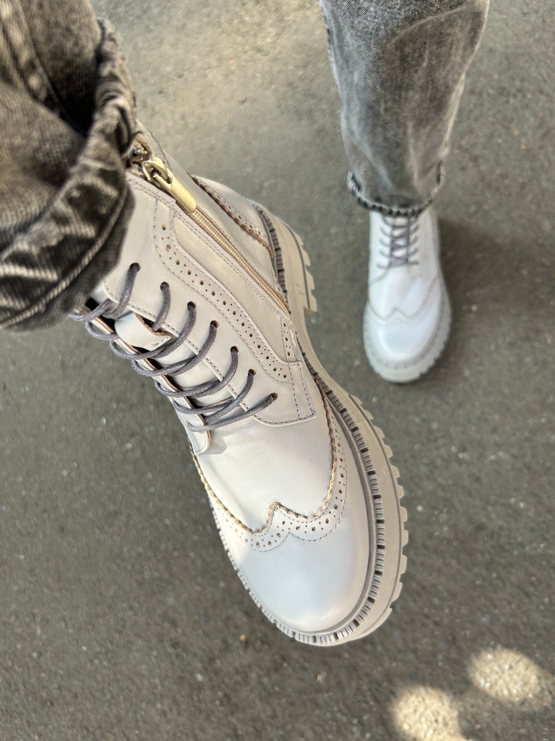 May include: White leather boots with a zipper and laces. The boots have a brogue design and a chunky sole.