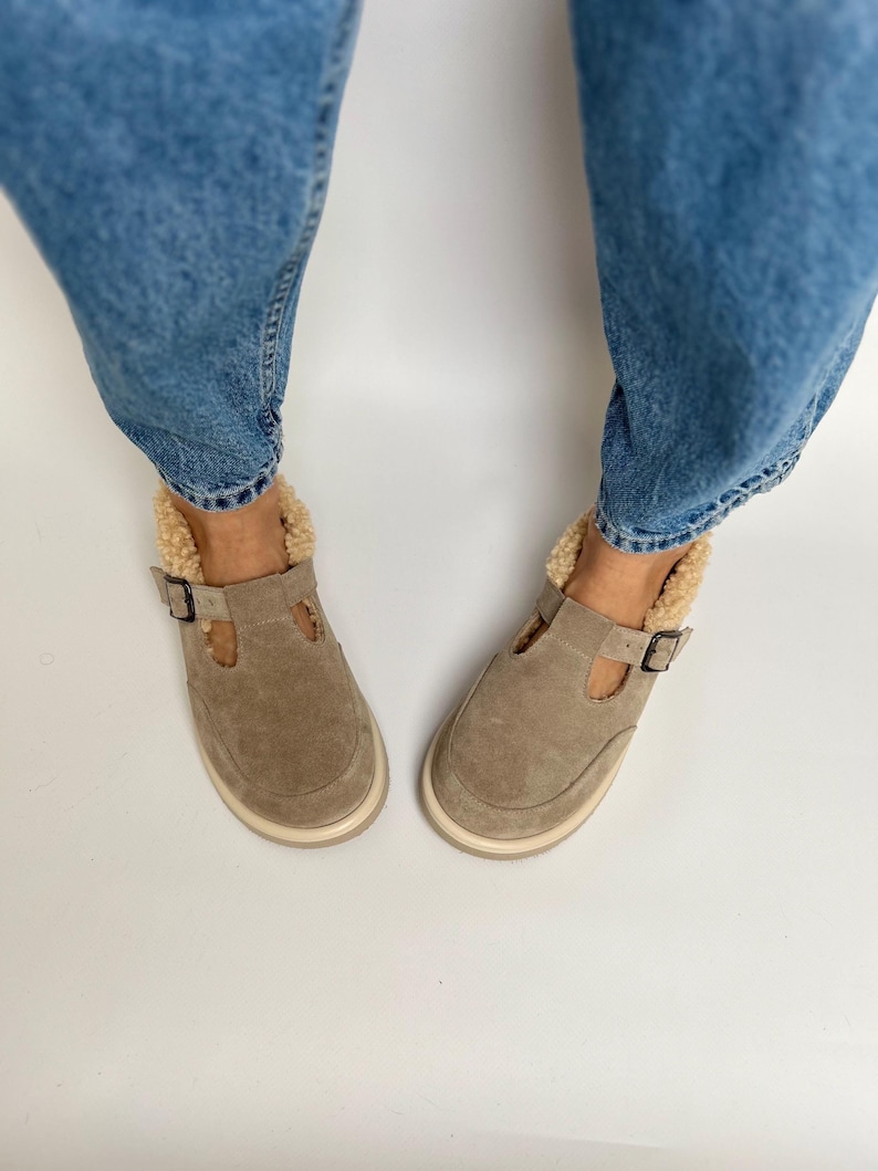 Puede incluir: Un par de zapatos de ante marr&oacute;n claro con cierre de hebilla y forro de piel sint&eacute;tica. Los zapatos son usados por una persona que lleva pantalones vaqueros azules.