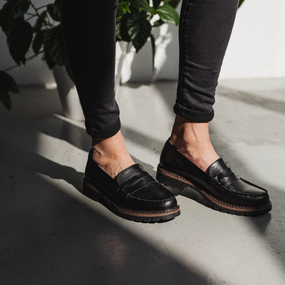A woman wearing black leather penny loafers.