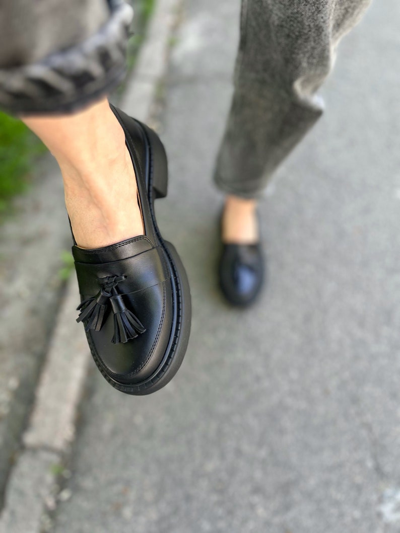 May include: Black leather loafers with a tassel detail. The loafers have a chunky platform sole.
