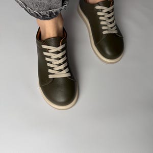 May include: A pair of green leather low-top sneakers with white laces. The sneakers have a white rubber sole.