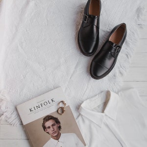 May include: A white shirt with a collar, a magazine titled "Kinfolk" featuring a man wearing a white shirt, and two black leather shoes with buckles.