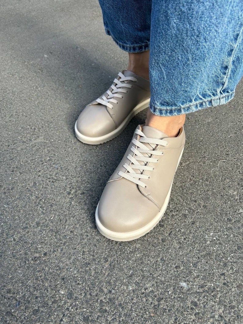 May include: A pair of light beige leather low-top sneakers with white laces and a white rubber sole.