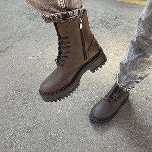 May include: Brown leather lace-up boots with a chunky sole and a zip on the side. The boots are worn with jeans.