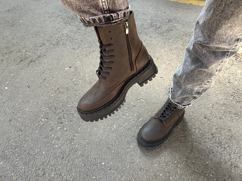 May include: Brown leather lace-up boots with a chunky sole and a zip on the side. The boots are worn with jeans.