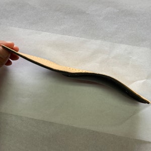 May include: A close-up of a brown leather wallet with a black lining. The wallet is folded in half and the inside is visible.