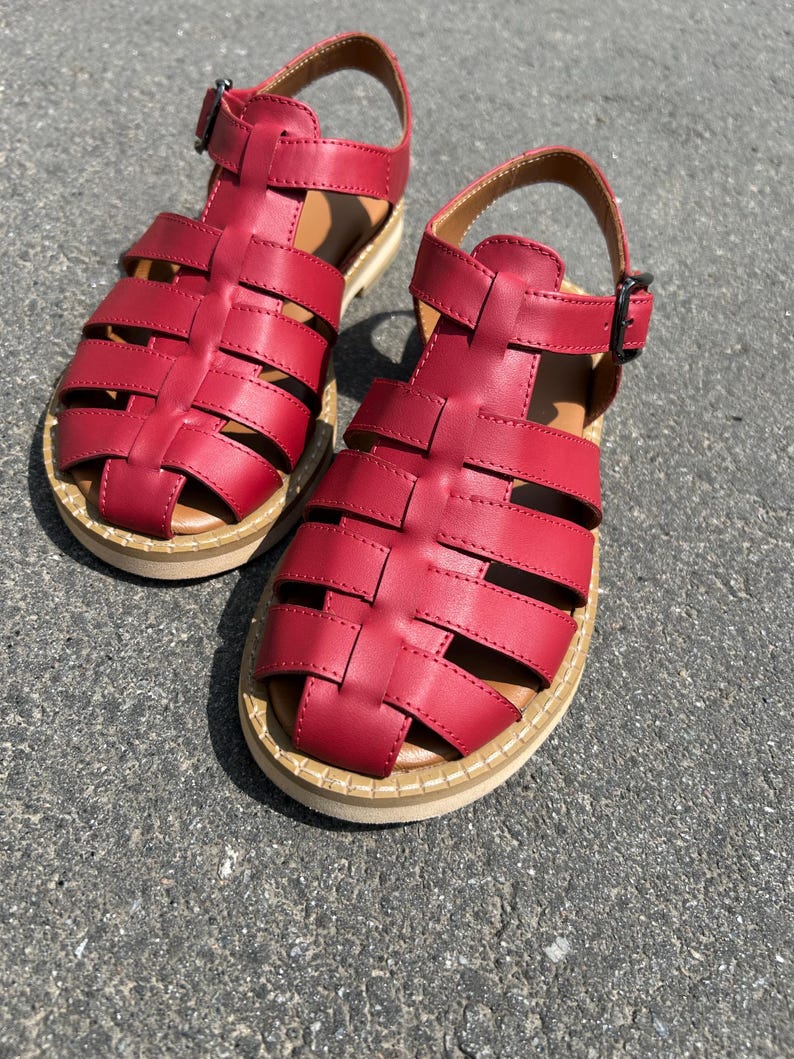 Puede incluir: Un par de sandalias de cuero rojo con un dise&ntilde;o tejido. Las sandalias tienen un cierre de hebilla y una suela beige. Las sandalias miden aproximadamente 20 cm de largo.