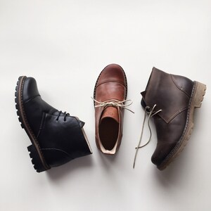 May include: Three pairs of leather ankle boots in brown, black, and dark brown. The boots have laces and are made of a soft, supple leather.