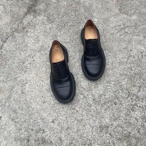 May include: A pair of black leather lace-up shoes with a chunky sole. The shoes have a classic oxford style and are made of high-quality leather.