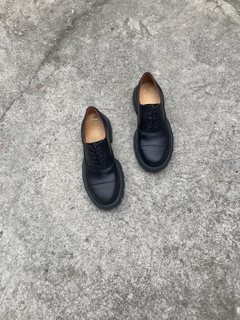 May include: A pair of black leather lace-up shoes with a chunky sole. The shoes have a classic oxford style and are made of high-quality leather.