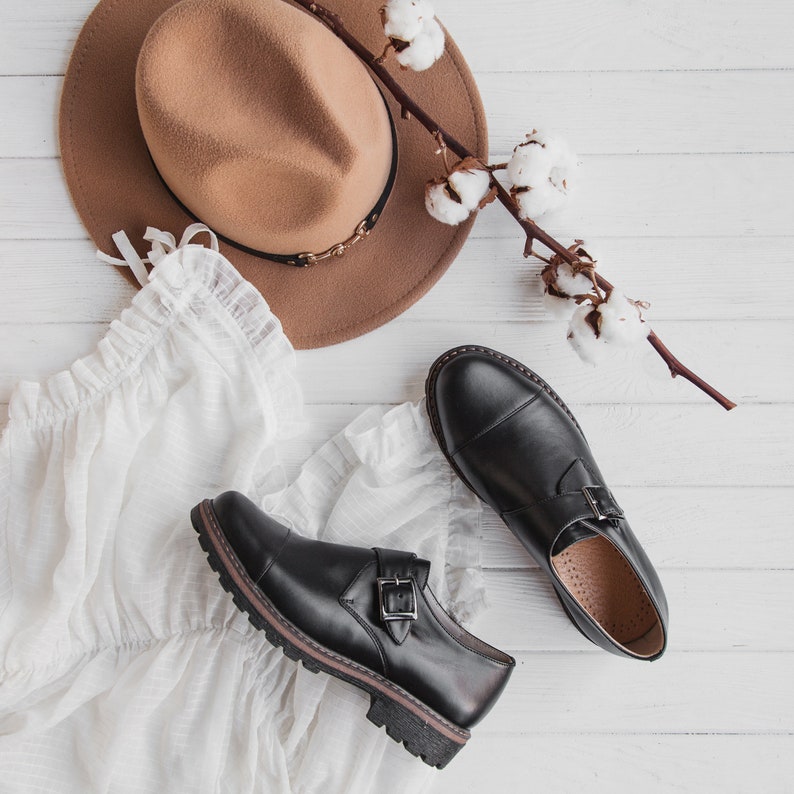 May include: A pair of black leather shoes with buckles, a brown fedora hat, and a white cotton fabric with a branch of cotton bolls.