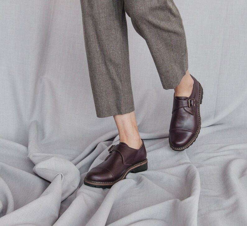 K&ouml;nnte beinhalten: Ein Paar braune Lederschnallen-Schuhe mit dicker Sohle. Die Schuhe werden von einer Person getragen, die eine braune Hose tr&auml;gt.