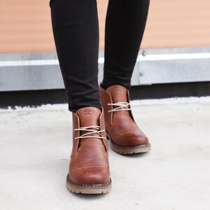 May include: A pair of brown leather ankle boots with white laces. The boots have a  "GOR" logo on the side.
