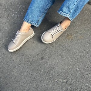 May include: A pair of light gray leather sneakers with white laces. The sneakers have a rounded toe and a white rubber sole.