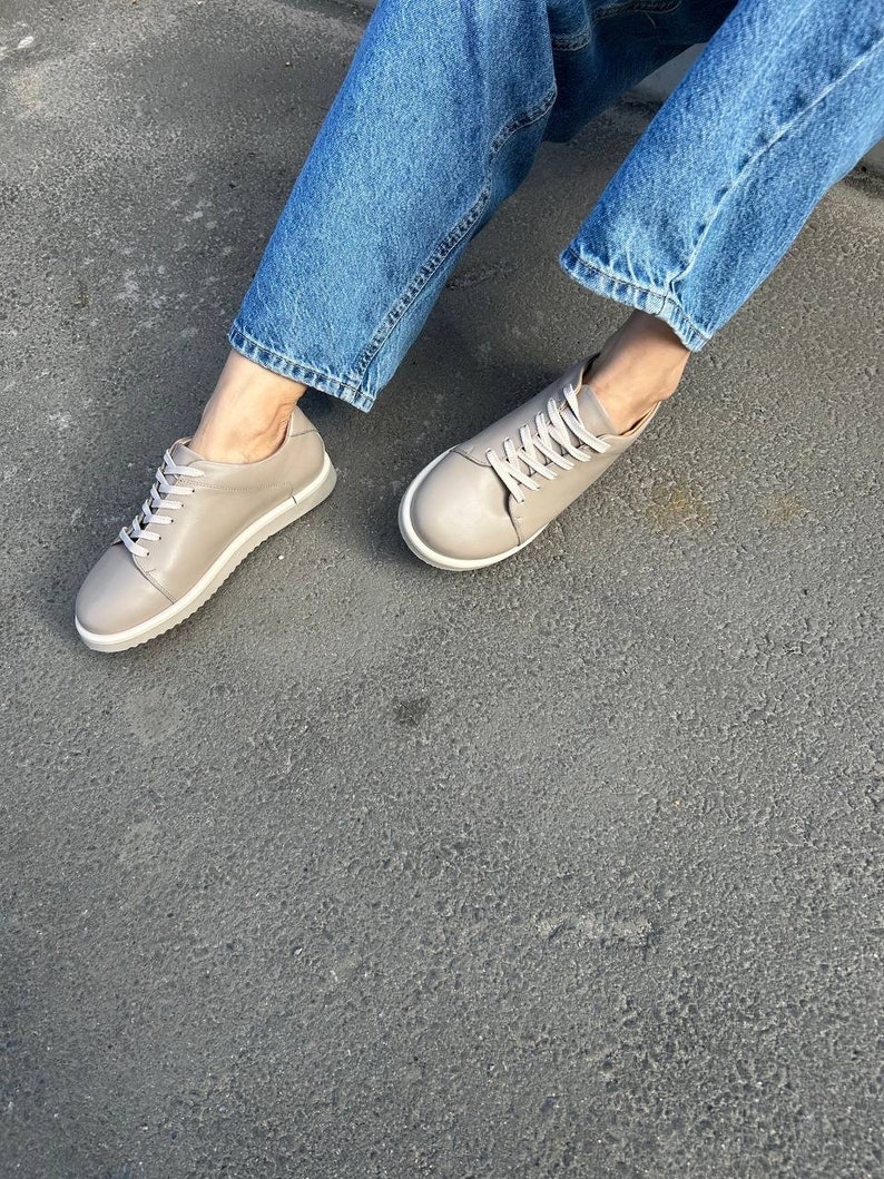 May include: A pair of light gray leather sneakers with white laces. The sneakers have a rounded toe and a white rubber sole.