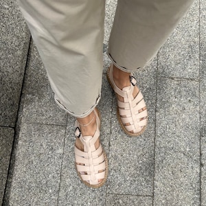 May include: A pair of light pink leather sandals with a woven design. The sandals have a buckle closure and a thick, flat sole.