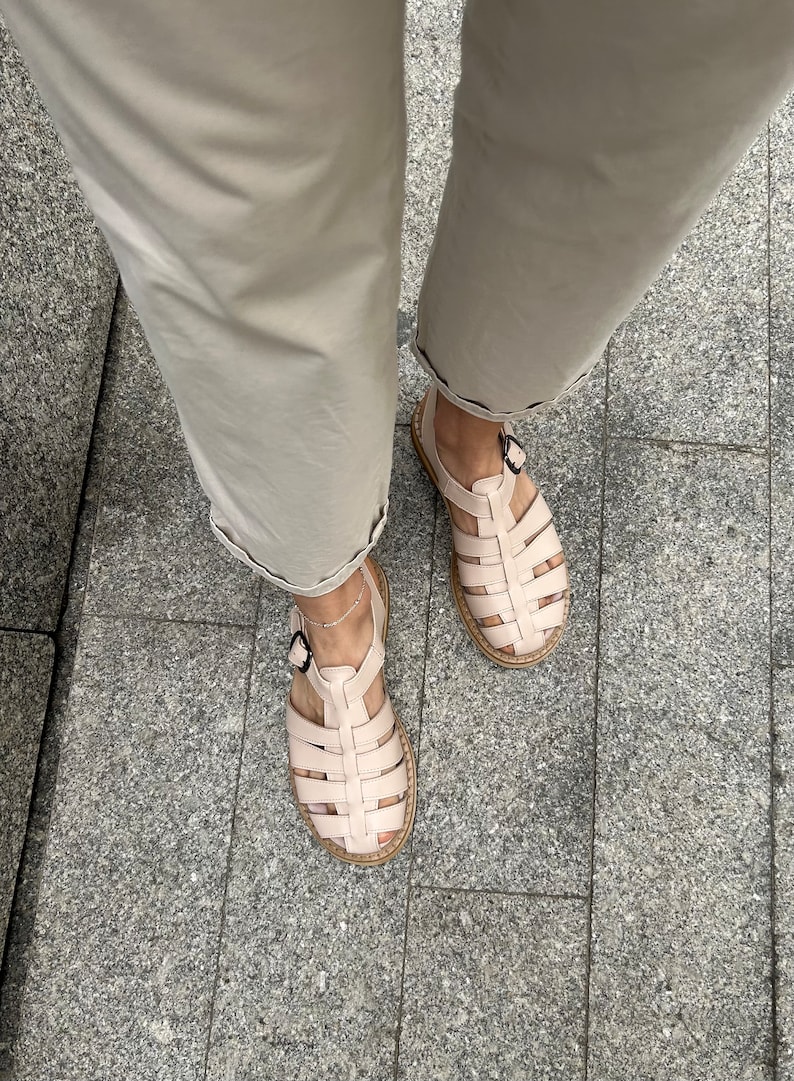 May include: A pair of light pink leather sandals with a woven design. The sandals have a buckle closure and a thick, flat sole.
