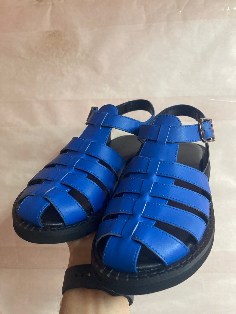 May include: A pair of blue leather sandals with a caged design and black soles.
